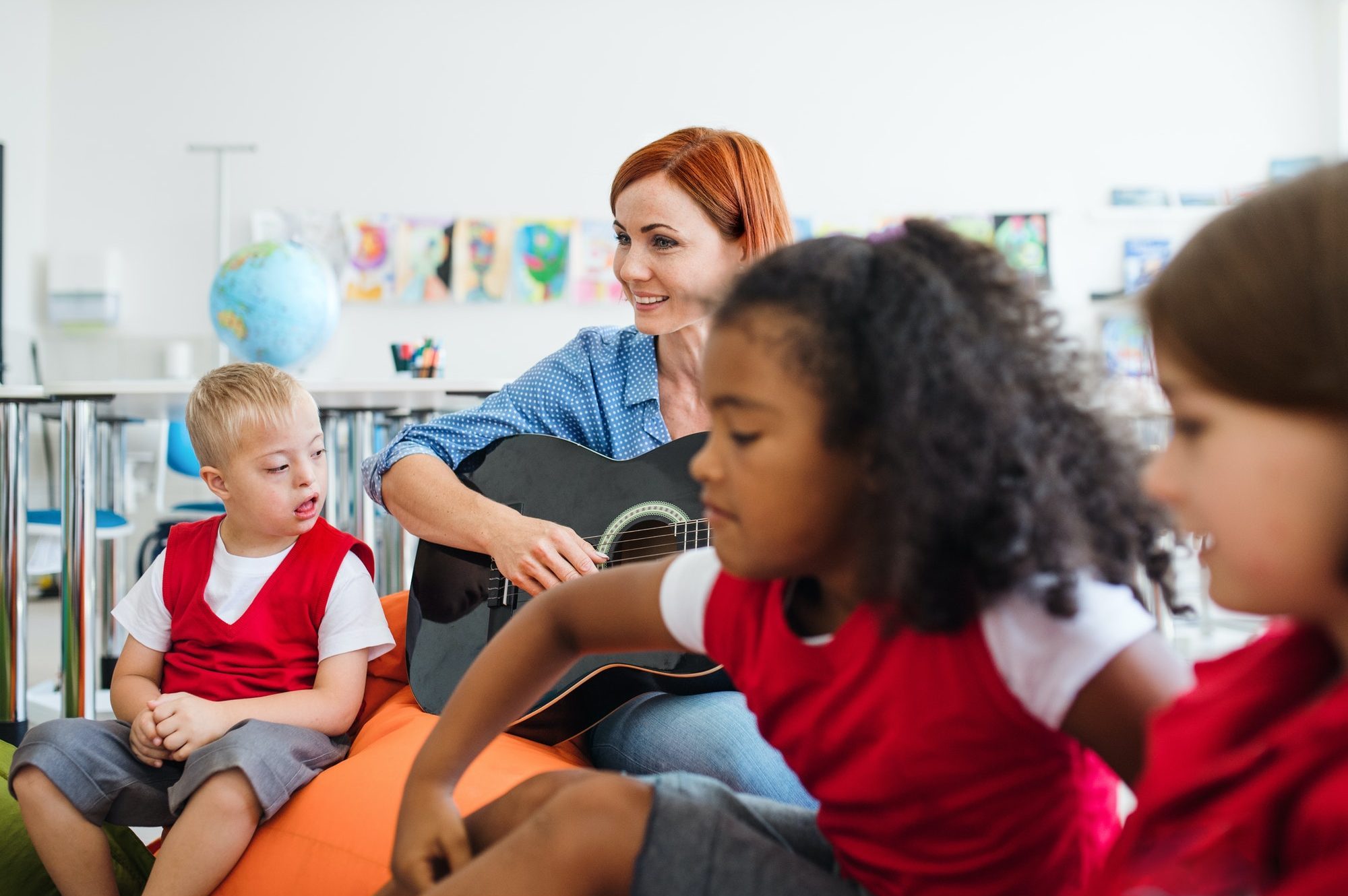 A group of small school kids and teacher with guitar sitting on the floor in class