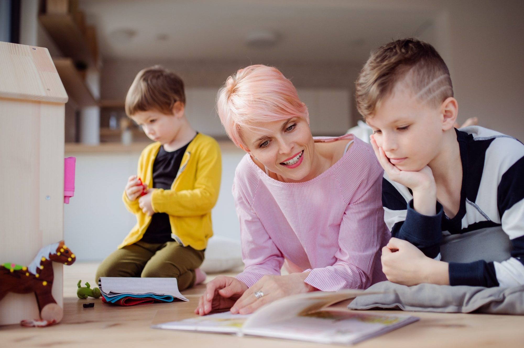 A young woman with two children reading book and playing on the floor.